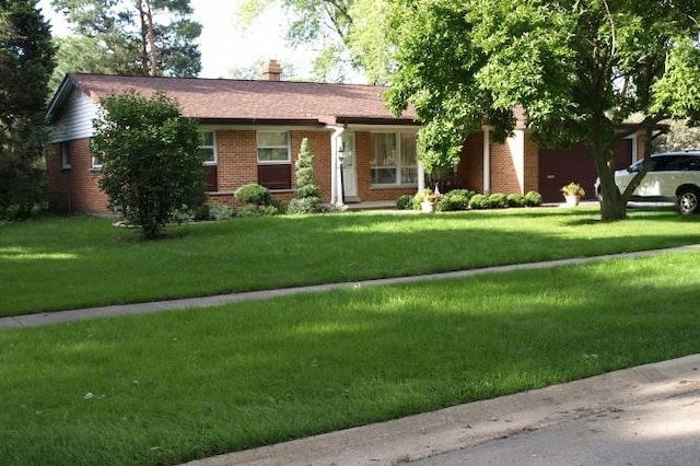 single story home with a chimney, an attached garage, a front yard, and brick siding