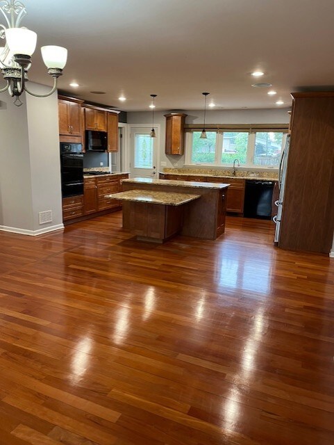 kitchen with brown cabinetry, dark wood-style flooring, a kitchen island, a sink, and black appliances