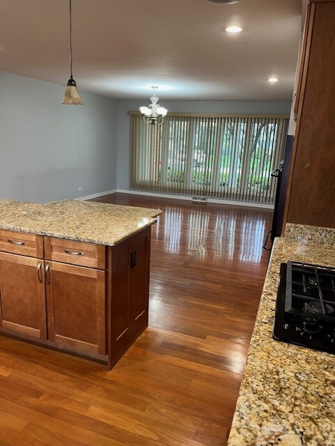 kitchen with decorative light fixtures, wood finished floors, black gas cooktop, light stone counters, and a notable chandelier