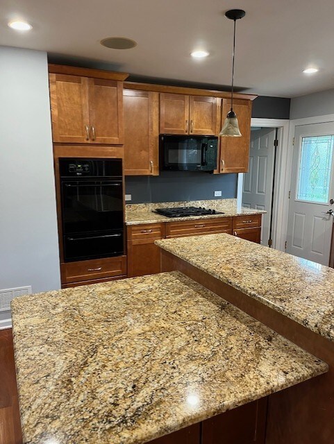 kitchen with brown cabinets, light stone counters, black appliances, wood finished floors, and a warming drawer