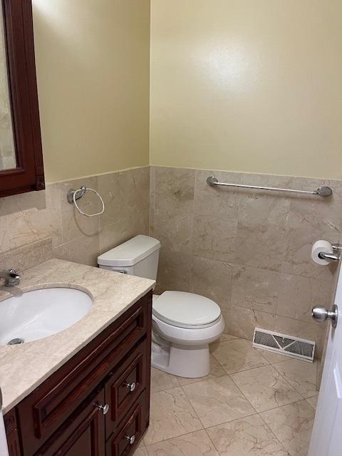 bathroom featuring tile walls, vanity, toilet, and visible vents
