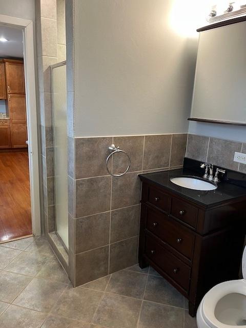 full bathroom featuring vanity, tile patterned floors, a wainscoted wall, tile walls, and a shower stall