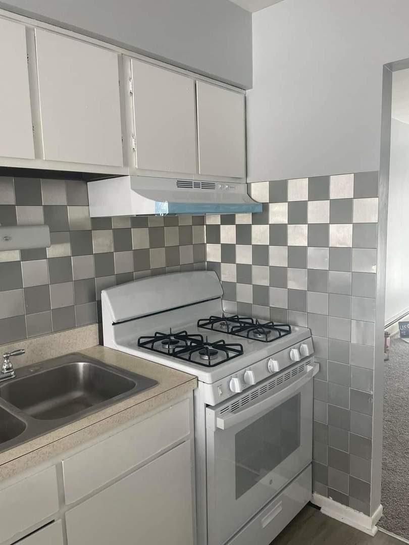 kitchen featuring white gas range, tasteful backsplash, light countertops, under cabinet range hood, and white cabinetry