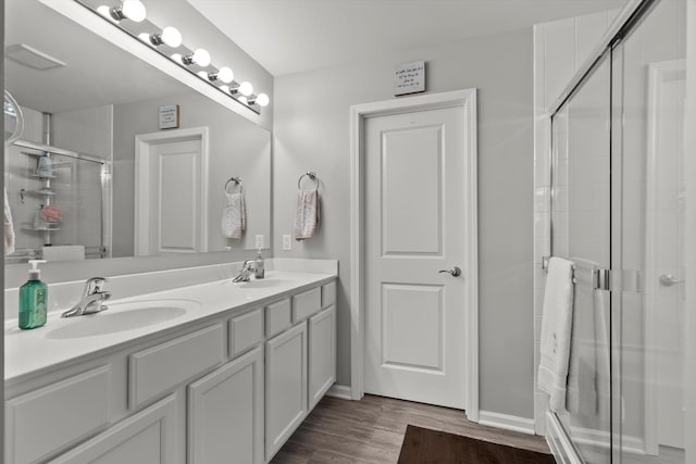 bathroom with wood finished floors, a sink, double vanity, and a shower stall