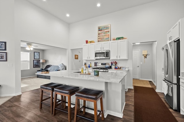 kitchen with a breakfast bar area, white cabinetry, dark wood-style floors, stainless steel appliances, and a towering ceiling