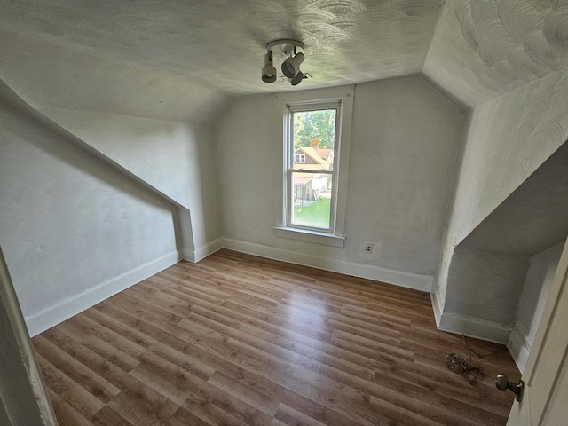 additional living space featuring baseboards, a textured ceiling, wood finished floors, and vaulted ceiling