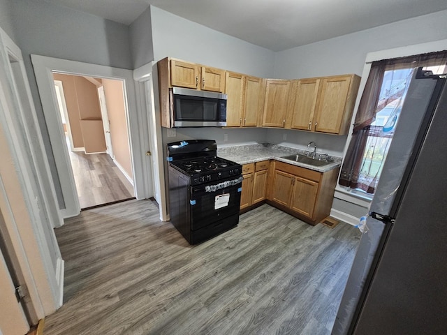 kitchen featuring light countertops, a sink, wood finished floors, appliances with stainless steel finishes, and baseboards