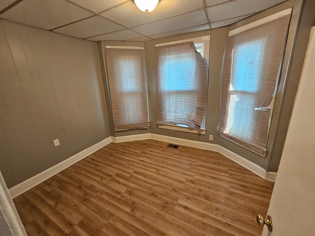 empty room featuring a paneled ceiling, wood finished floors, plenty of natural light, and visible vents