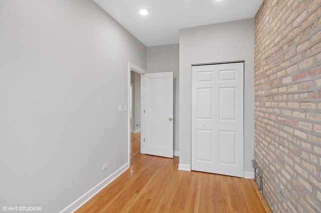 unfurnished bedroom featuring a closet, baseboards, recessed lighting, light wood-style floors, and brick wall