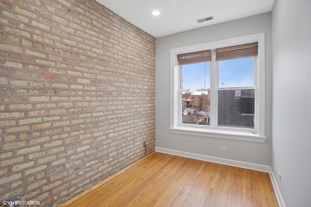 unfurnished room with light wood-style flooring, baseboards, brick wall, and visible vents
