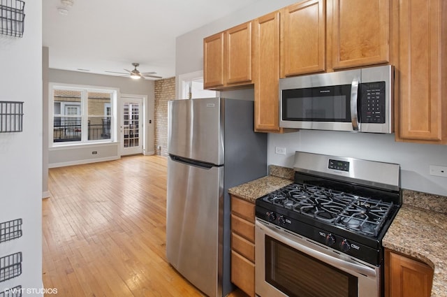 kitchen featuring baseboards, light wood-style floors, ceiling fan, light stone countertops, and appliances with stainless steel finishes