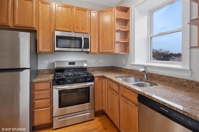 kitchen featuring open shelves, stainless steel appliances, a sink, light wood-style floors, and stone countertops