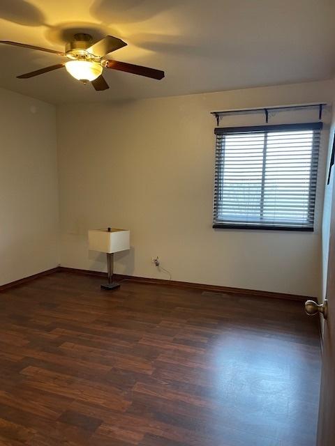 empty room with baseboards, ceiling fan, and dark wood-type flooring