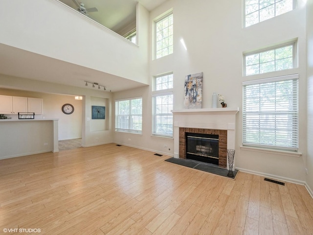 unfurnished living room featuring a towering ceiling, a tiled fireplace, light wood-type flooring, baseboards, and ceiling fan