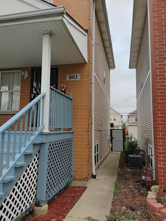 doorway to property featuring a porch, brick siding, and central air condition unit