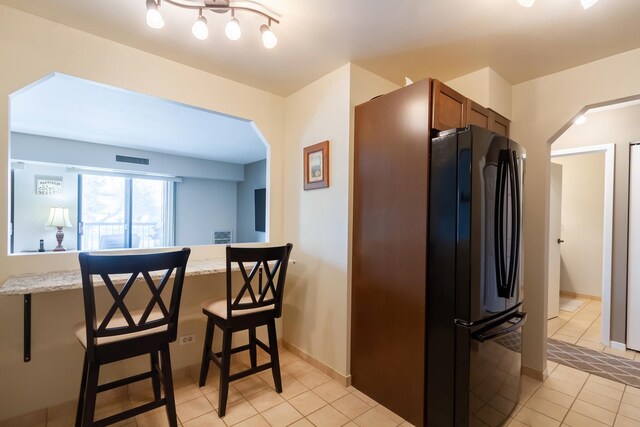 1505 E Central Rd Unit 211B, Arlington Heights, IL 60005 - kitchen with freestanding refrigerator, arched walkways, light tile patterned floors, brown cabinets, and a breakfast bar