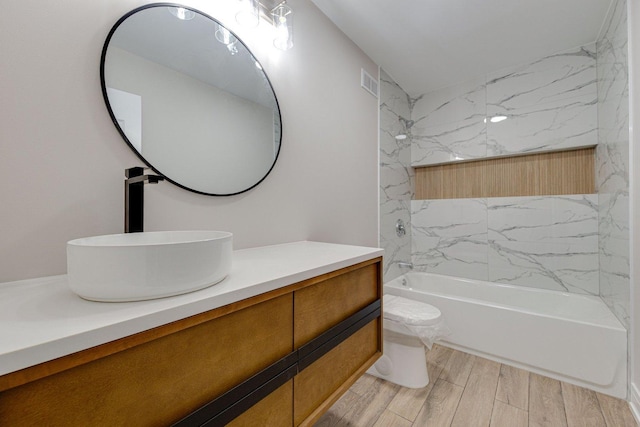 bathroom with visible vents, toilet, wood finish floors, vanity, and bathing tub / shower combination