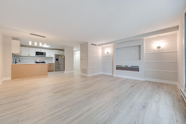 unfurnished living room featuring baseboards, light wood-type flooring, a sink, and a glass covered fireplace