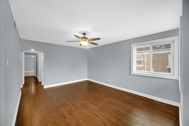 unfurnished room featuring visible vents, baseboards, arched walkways, a ceiling fan, and dark wood-style floors