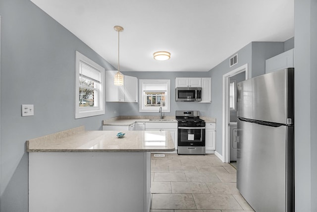 kitchen with a peninsula, white cabinets, appliances with stainless steel finishes, a sink, and hanging light fixtures