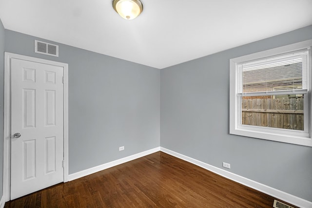 empty room featuring baseboards, dark wood-style floors, and visible vents