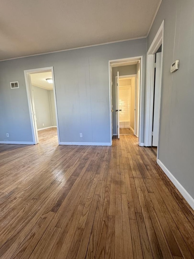 empty room with hardwood / wood-style floors, visible vents, baseboards, and ornamental molding