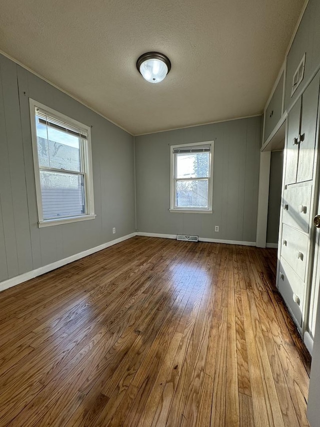interior space with visible vents, a textured ceiling, baseboards, and wood finished floors