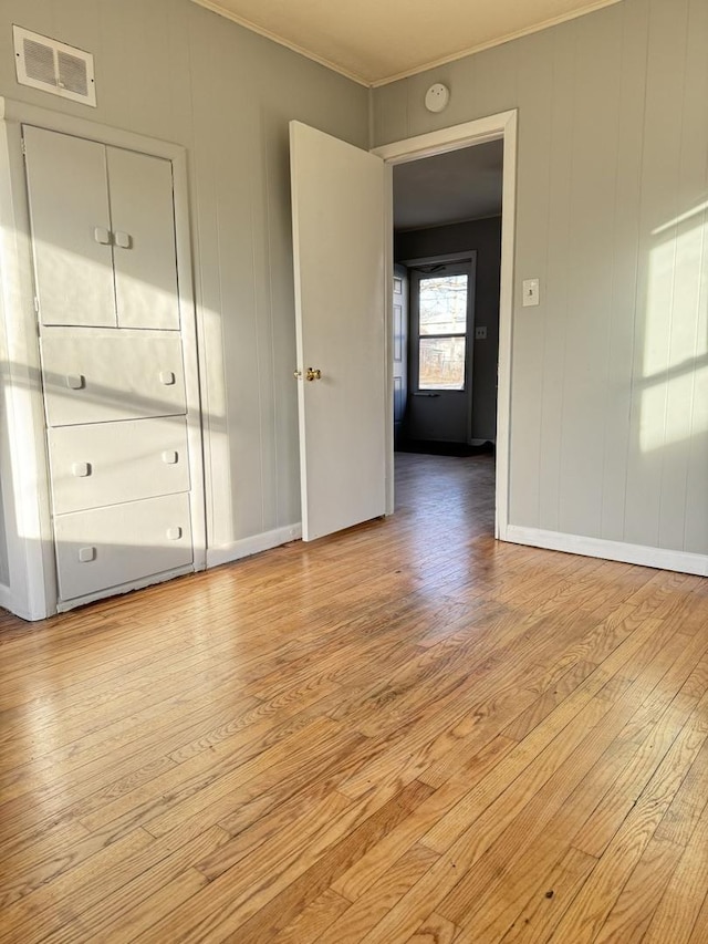 empty room featuring light wood finished floors, visible vents, baseboards, and crown molding