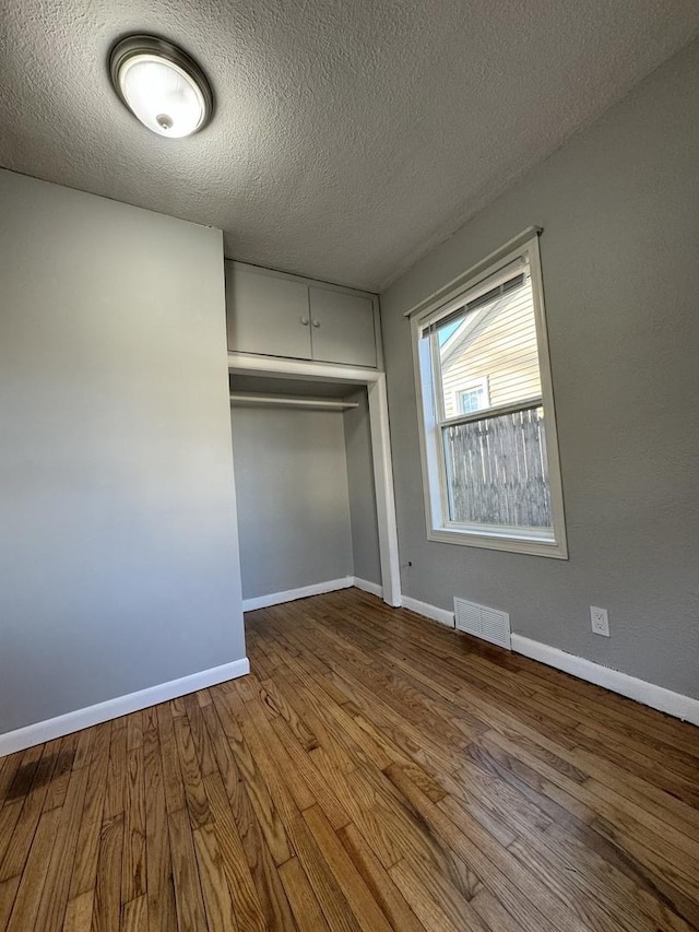 unfurnished bedroom with visible vents, a closet, baseboards, and wood finished floors