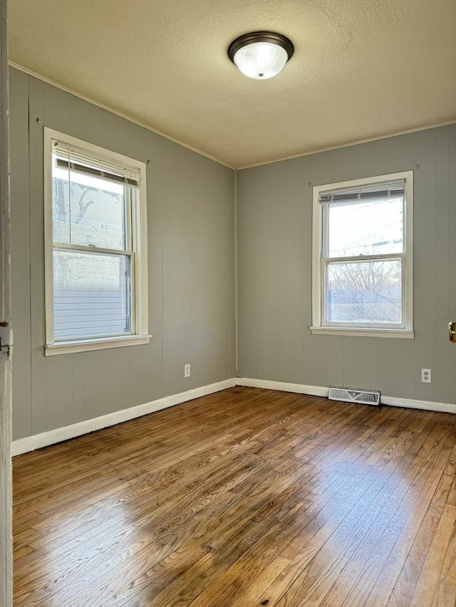 spare room featuring baseboards, visible vents, a textured ceiling, and hardwood / wood-style floors