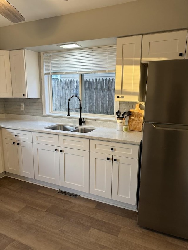 kitchen featuring freestanding refrigerator, a sink, white cabinetry, and visible vents