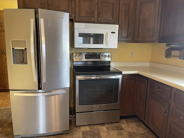 kitchen featuring light countertops, stainless steel appliances, dark brown cabinets, and stone finish flooring