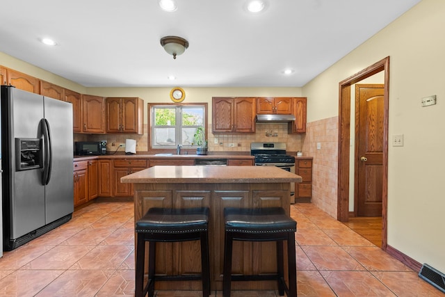 3315 E Bemes Rd, Crete, IL 60417 - kitchen with appliances with stainless steel finishes, a kitchen island, under cabinet range hood, a breakfast bar area, and tasteful backsplash