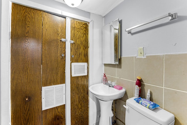 bathroom with toilet, a sink, tile walls, and visible vents