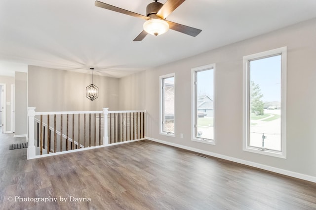unfurnished room with visible vents, ceiling fan with notable chandelier, baseboards, and wood finished floors