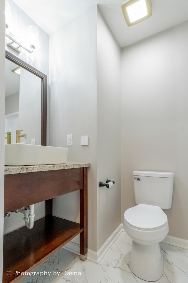 half bath featuring baseboards, marble finish floor, toilet, and a sink