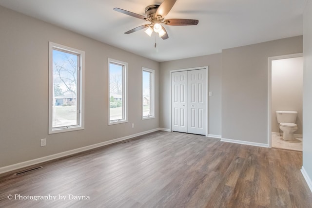 unfurnished bedroom featuring ensuite bathroom, baseboards, visible vents, a closet, and wood finished floors
