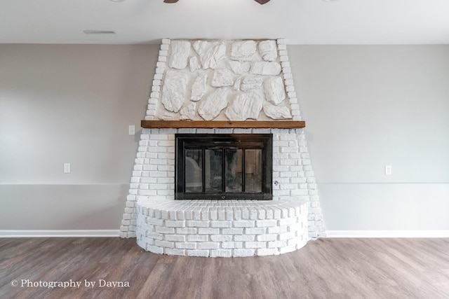 room details with a large fireplace, visible vents, baseboards, ceiling fan, and wood finished floors