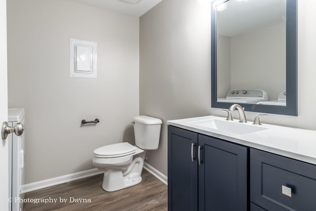 half bathroom with washer and clothes dryer, toilet, vanity, wood finished floors, and baseboards