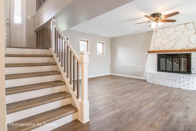 staircase with baseboards, wood finished floors, a glass covered fireplace, and a ceiling fan