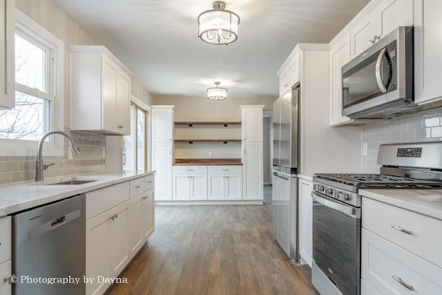 kitchen featuring light countertops, a sink, open shelves, wood finished floors, and stainless steel appliances