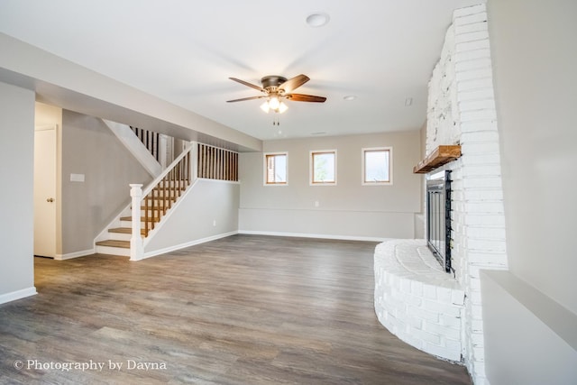 unfurnished living room with stairs, ceiling fan, a fireplace, and wood finished floors