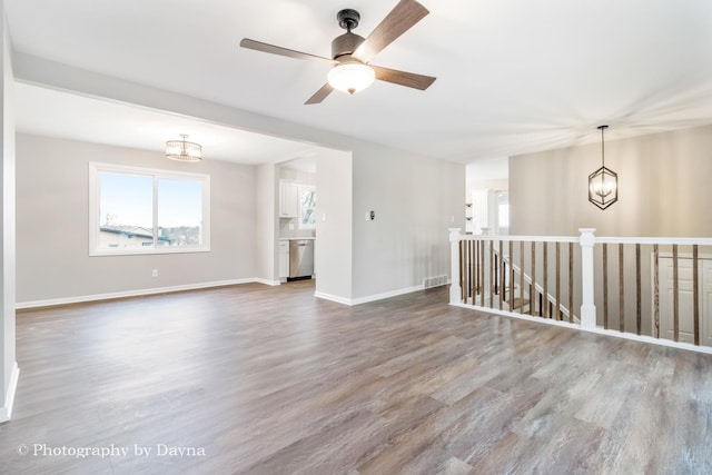 unfurnished living room featuring visible vents, ceiling fan with notable chandelier, baseboards, and wood finished floors