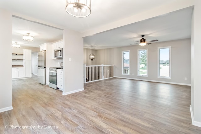 unfurnished living room with baseboards, ceiling fan with notable chandelier, and light wood finished floors