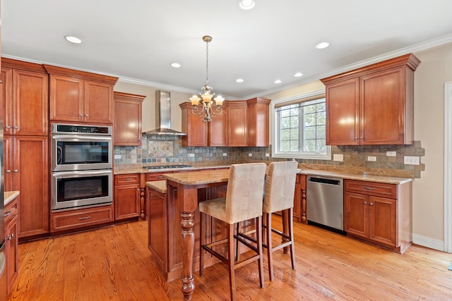 kitchen featuring wall chimney range hood, appliances with stainless steel finishes, an inviting chandelier, and light wood-style floors