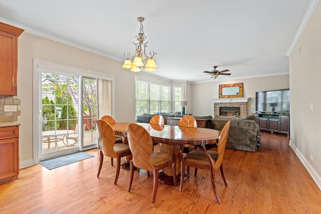 dining space featuring crown molding, a fireplace, baseboards, ceiling fan with notable chandelier, and light wood finished floors