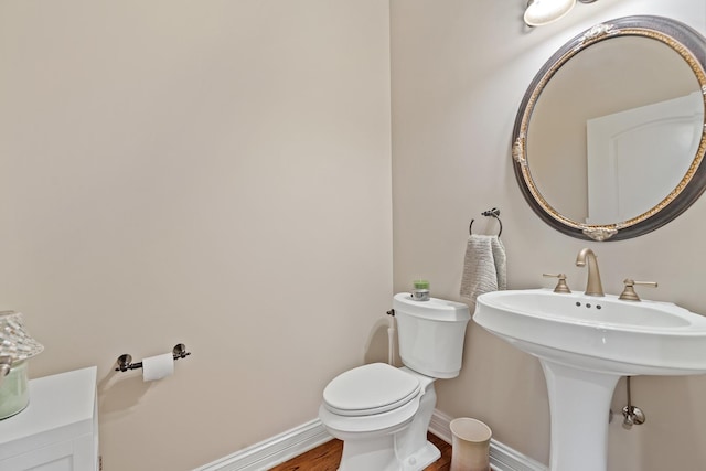 half bathroom featuring toilet, baseboards, and wood finished floors