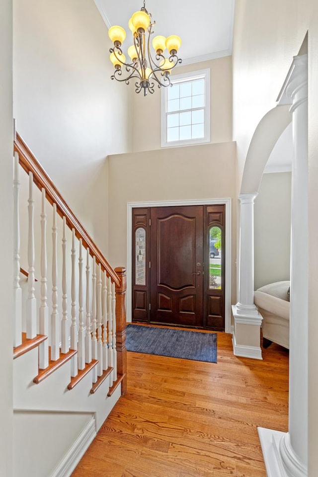 foyer featuring wood finished floors, ornamental molding, a high ceiling, and a chandelier