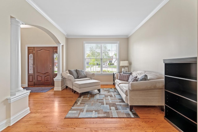 living area featuring crown molding, arched walkways, baseboards, decorative columns, and wood finished floors