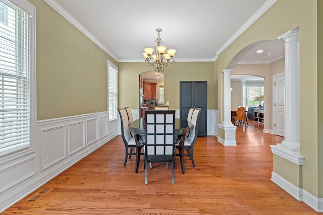 dining space with crown molding, arched walkways, light wood-style flooring, decorative columns, and visible vents